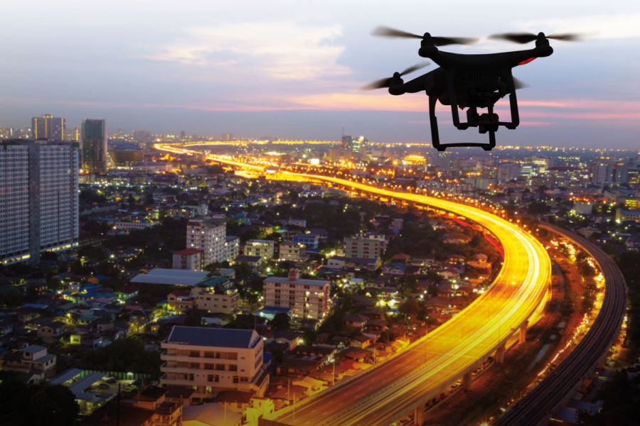 Silueta de drones sobrevolando una ciudad al anochecer.