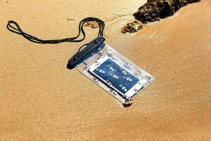 Teléfono móvil en funda de plástico sobre la arena de una playa.