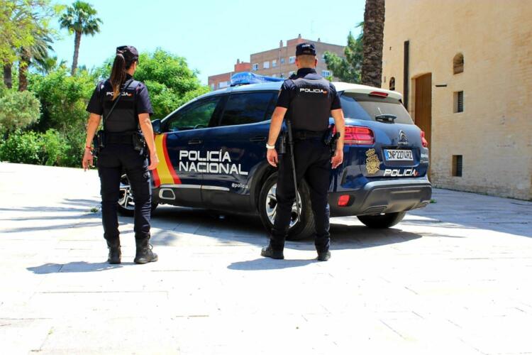 Una policía mujer y un policía hombre uniformados y de espaldas ante un coche de la Policía Nacional