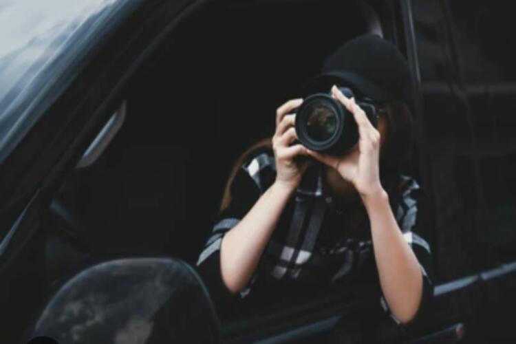 Mujer con camisa de cuadros oscura sostiene una cámara de fotos que le tapa la cara.