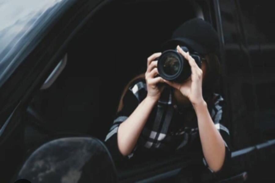 Mujer con camisa de cuadros oscura sostiene una cámara de fotos que le tapa la cara.
