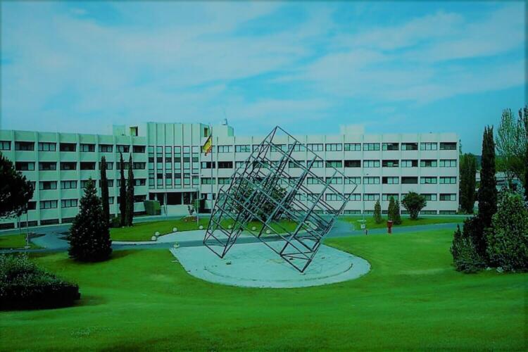 Escultura geométrica ante edificio blanco de cinco plantas rodeado de césped
